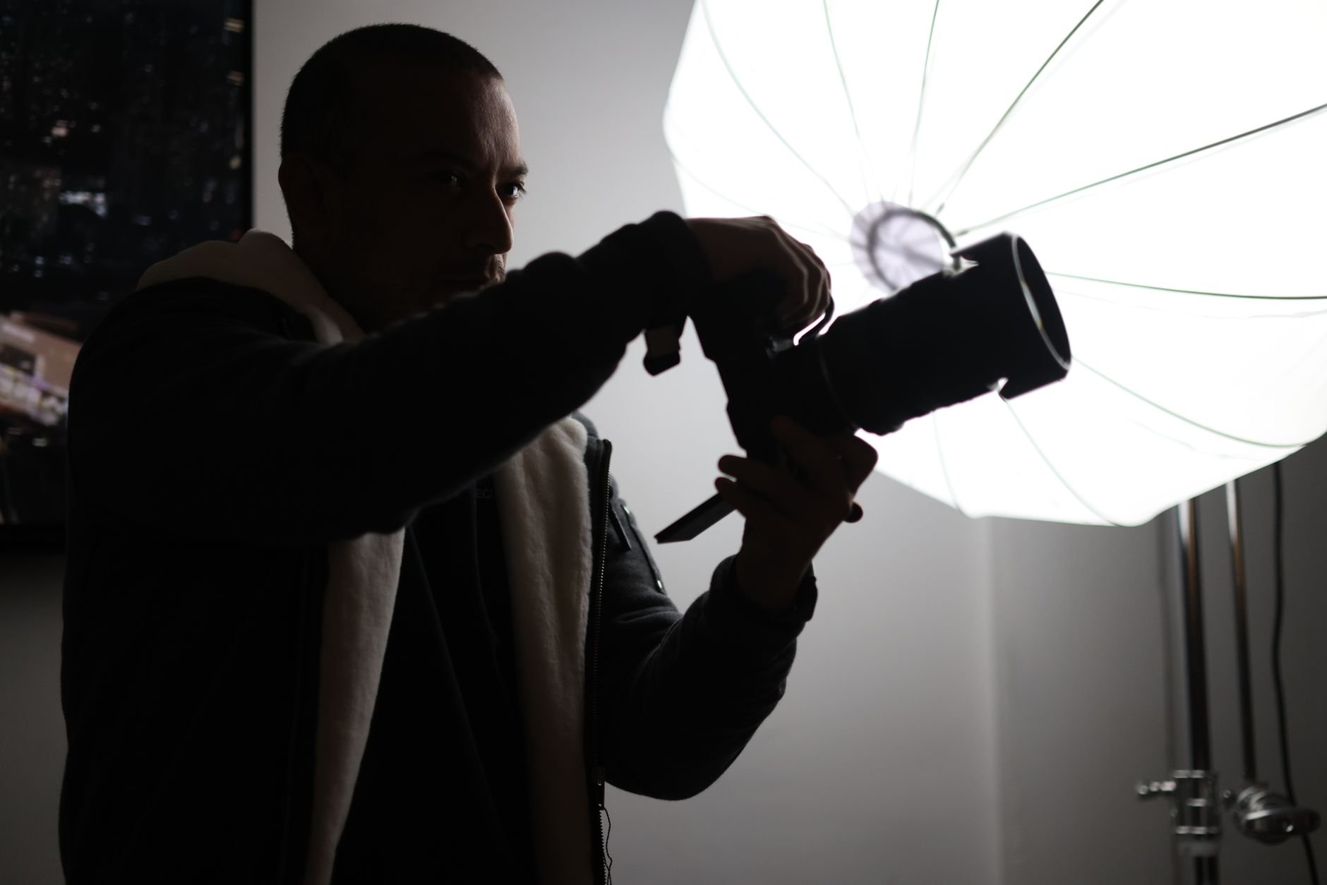 Silhouette of a photographer adjusting a camera during a studio shoot with a large umbrella light.