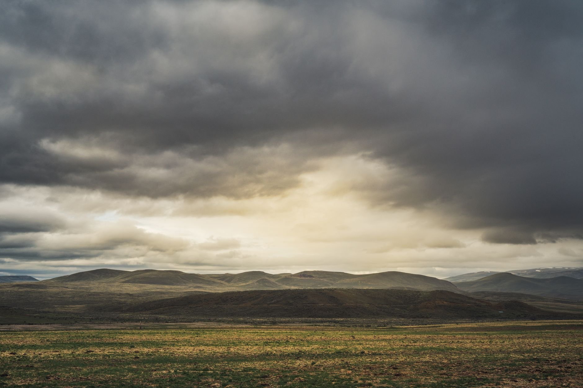 Dramatic landscape with rolling hills under a thick overcast sky providing a moody atmosphere.